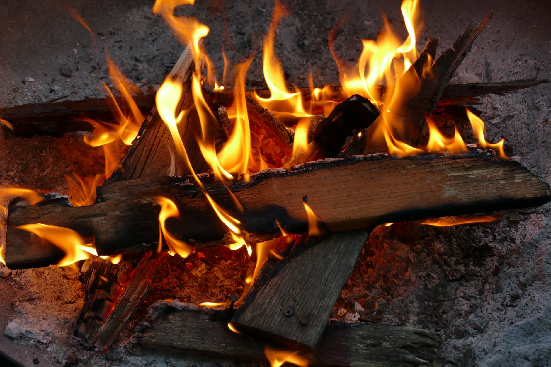 Žeravé drevo v ohnisku s vysokými plameňmi a praskajúcimi polenami na kamennom pozadí.